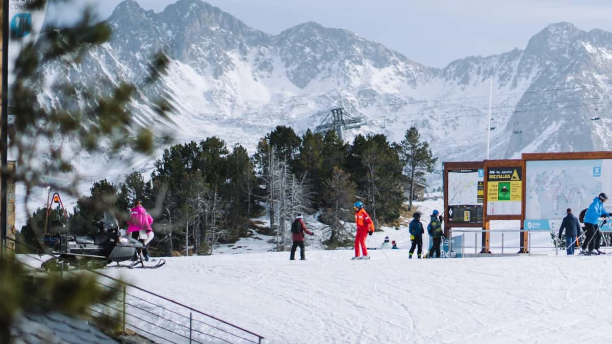 Bas des pistes à Soldeu en Andorre, un moniteur et de jeunes skieurs devant le panneau de risque d'avalanche