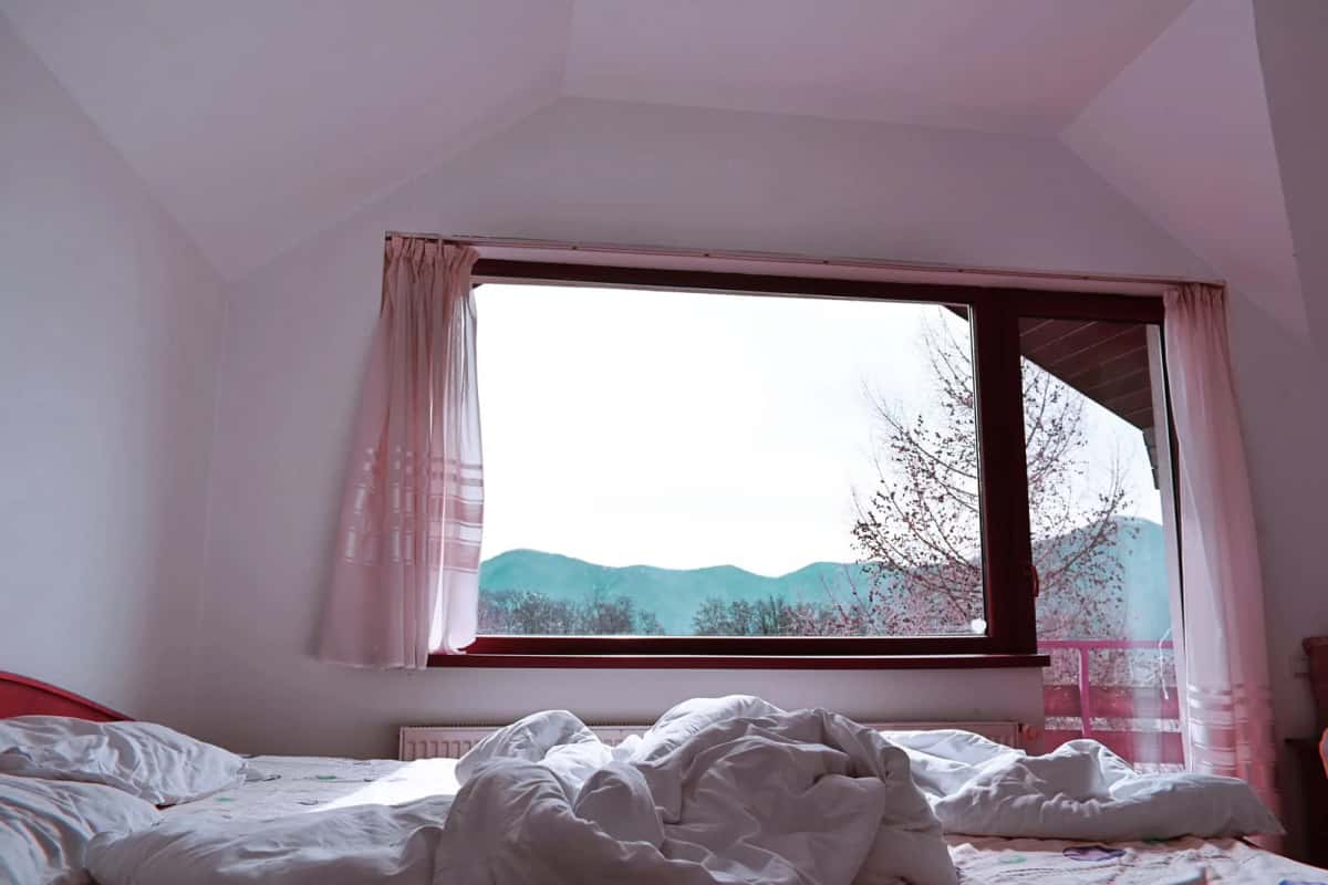 Chambre d'hôtel lumineuse avec une grande fenêtre ouverte sur les montagnes