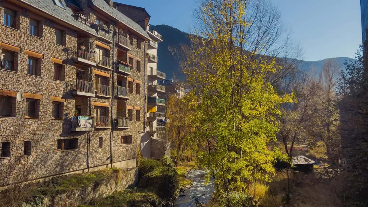 Immeuble d'habitation andorran en pierre, ses balcons surplombant un torrent, un versant boisé au fond