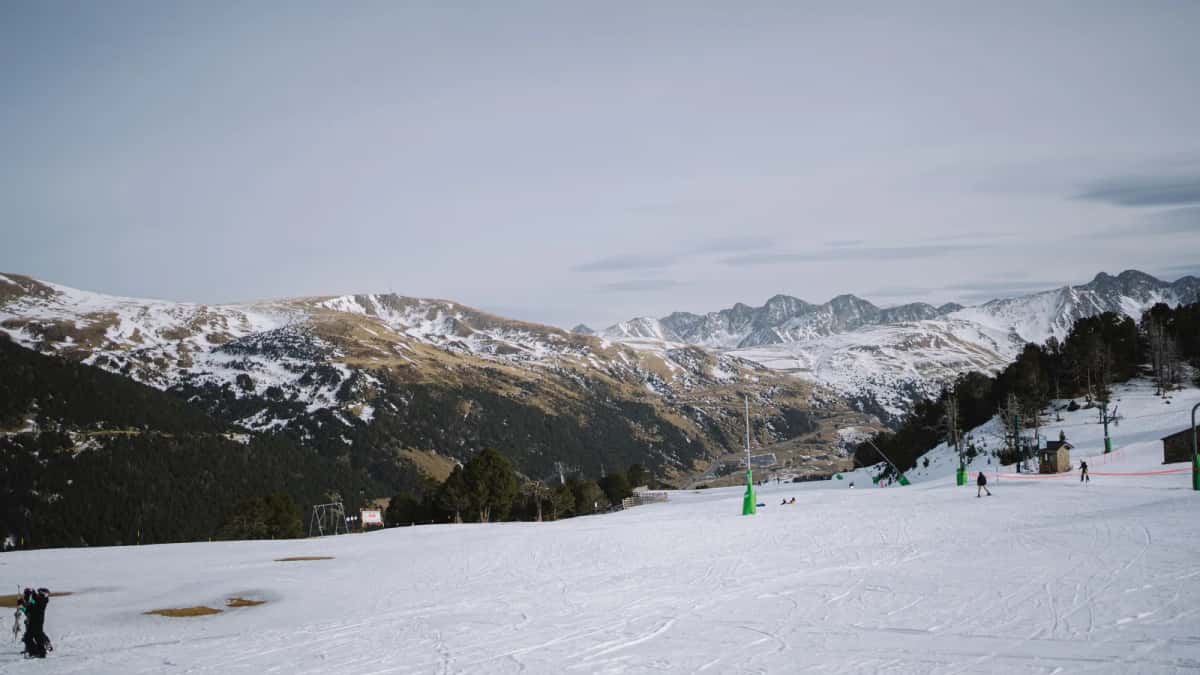 Piste damée d'un domaine andorran laissant apparaître des plaques dénudées, canons à neige et versants pelés au fond