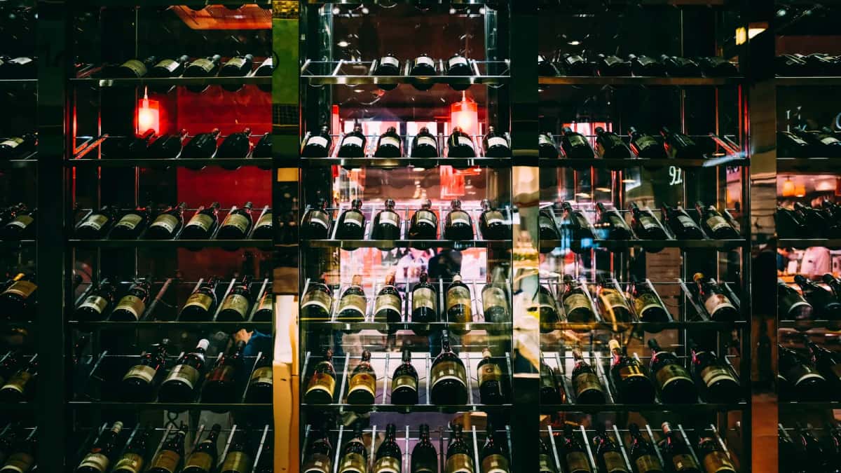 Mur de bouteilles alignées sur des étagères vitrées, étiquettes non lisibles