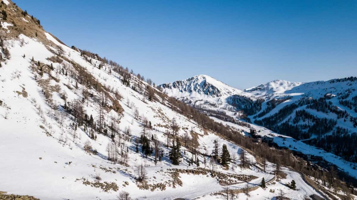 Versant enneigé d'une vallée de montagne en hiver, avec une route sinueuse au fond
