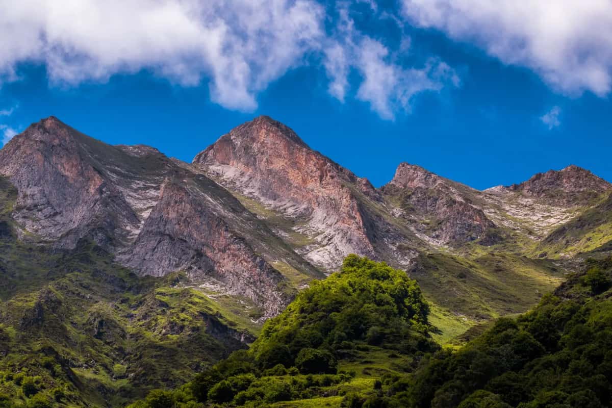 Sommets rocheux des Pyrénées aux versants verdoyants sous un ciel d'été