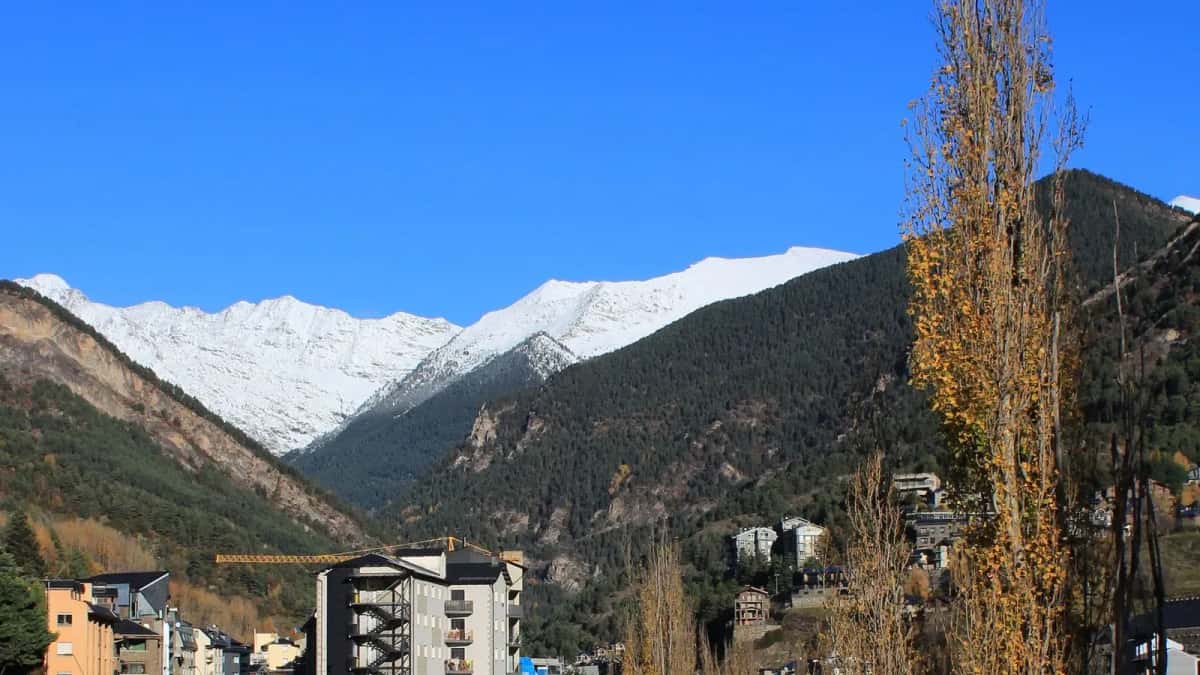 Vallée de La Massana en automne, la route longeant les immeubles et les crêtes enneigées au fond